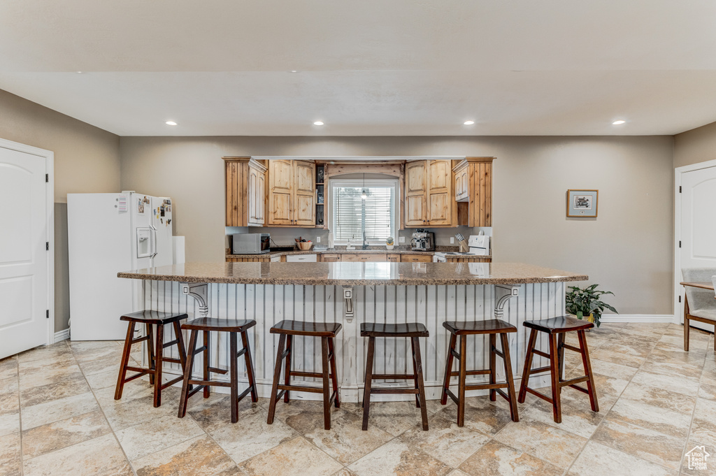 Kitchen with white refrigerator with ice dispenser, range, recessed lighting, a breakfast bar, and light stone finish floors