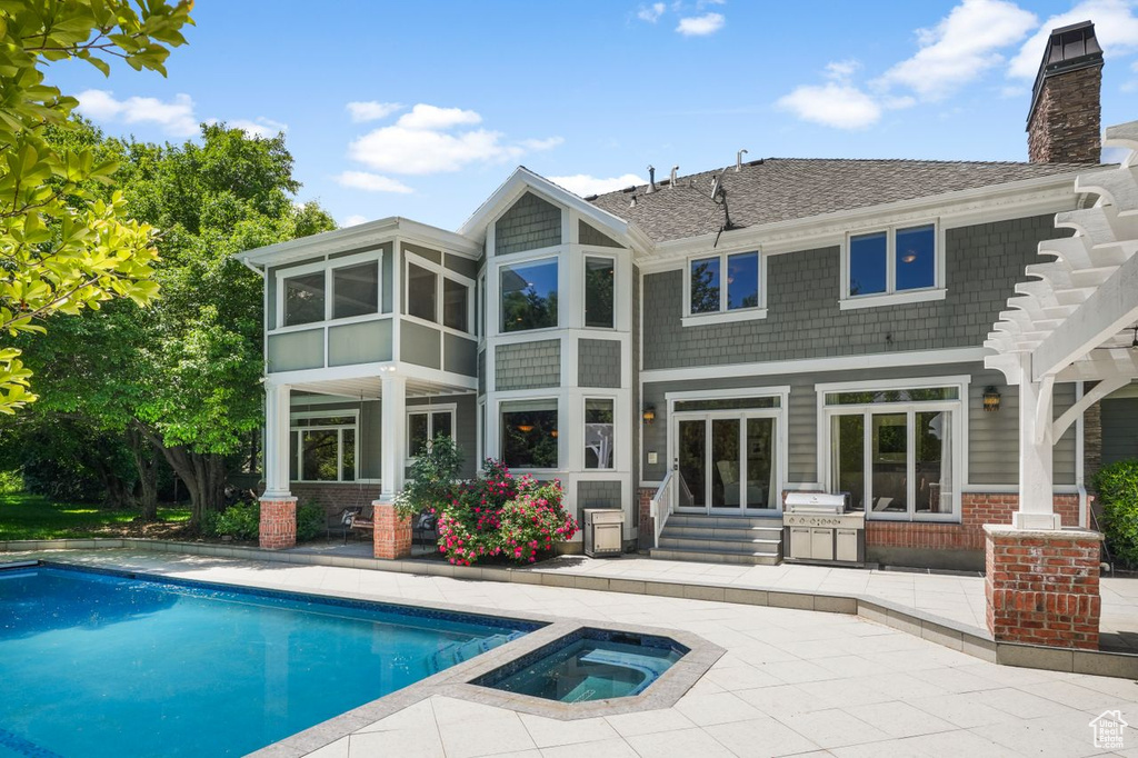 Back of house featuring a swimming pool with hot tub, a patio, and a pergola