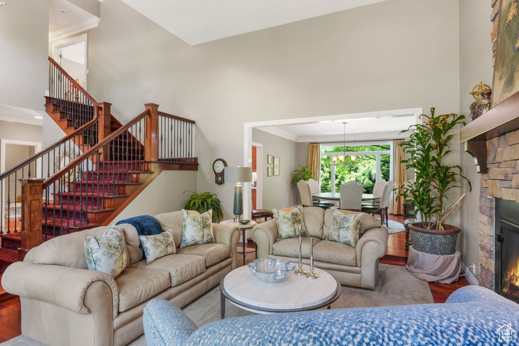 Living room with crown molding, hardwood / wood-style flooring, a towering ceiling, and a stone fireplace