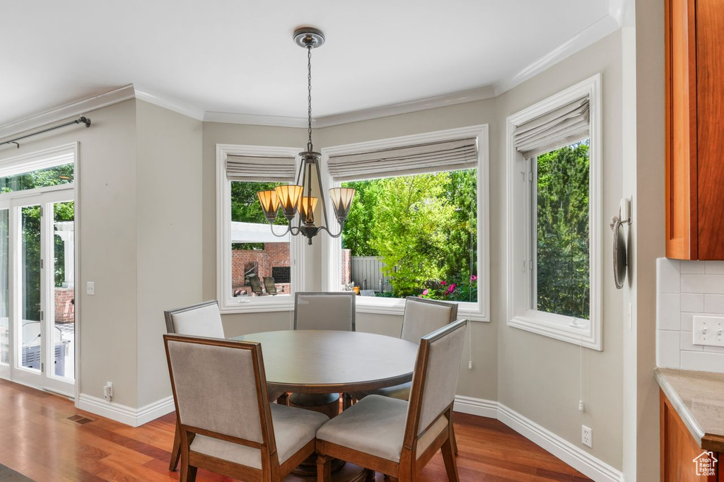 Dining space with hardwood / wood-style flooring, a wealth of natural light, a notable chandelier, and ornamental molding