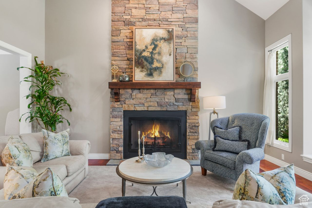 Living room featuring a healthy amount of sunlight, light hardwood / wood-style flooring, vaulted ceiling, and a stone fireplace