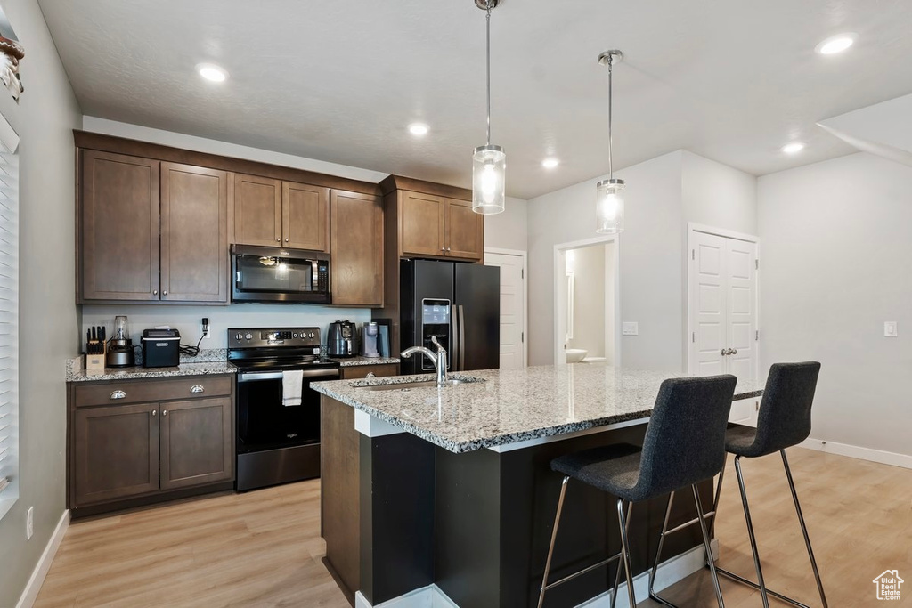 Kitchen with black appliances, a sink, light wood-style flooring, a kitchen breakfast bar, and baseboards