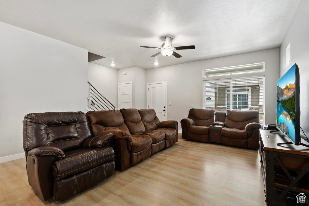 Living area featuring light wood-style floors, ceiling fan, stairs, and baseboards