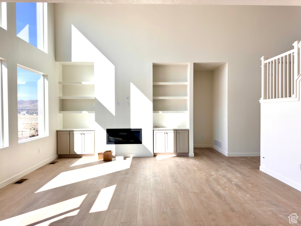 Unfurnished living room featuring a high ceiling, baseboards, visible vents, and light wood finished floors