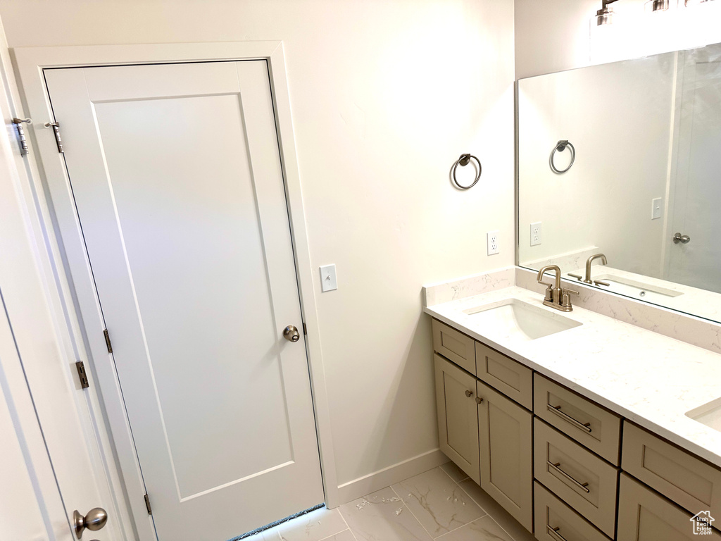 Full bathroom featuring double vanity, marble finish floor, baseboards, and a sink