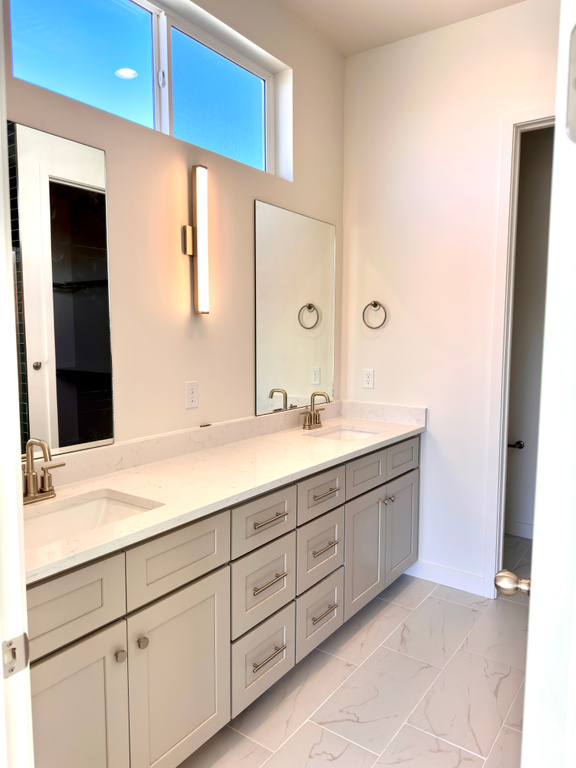 Bathroom featuring double vanity, marble finish floor, baseboards, and a sink