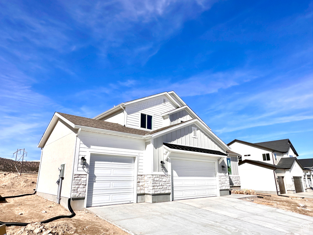 View of front of home with concrete driveway, an attached garage, stone siding, and a shingled roof