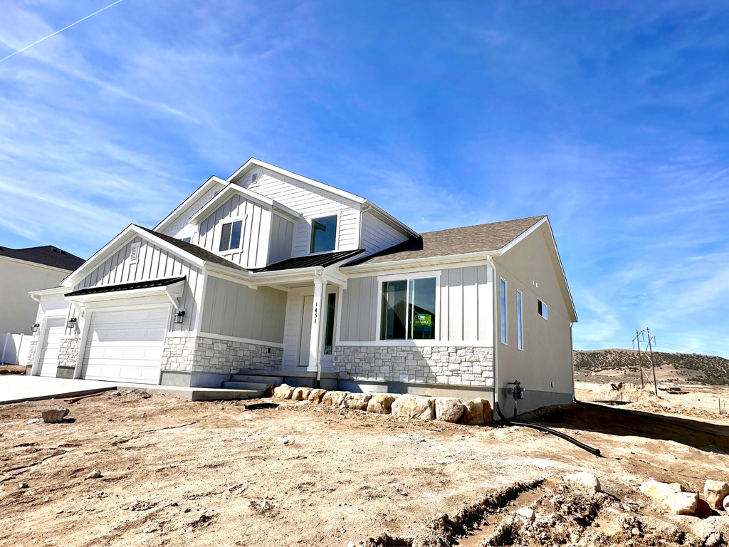 View of front of house featuring a garage, stone siding, and board and batten siding