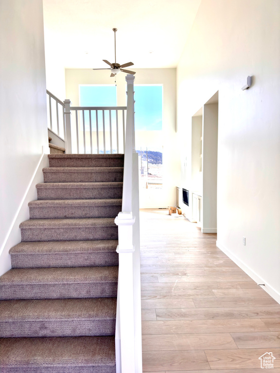 Staircase with ceiling fan, baseboards, wood finished floors, and a fireplace