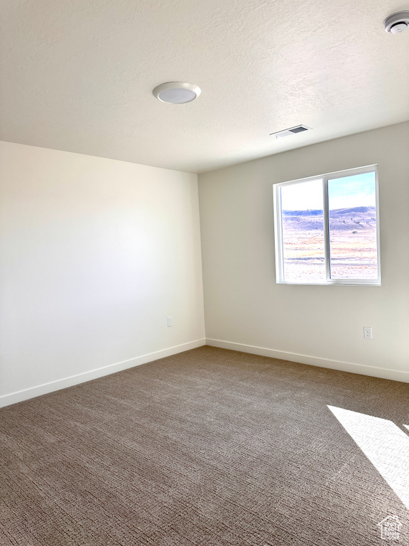 Unfurnished room with visible vents, baseboards, a textured ceiling, and dark carpet