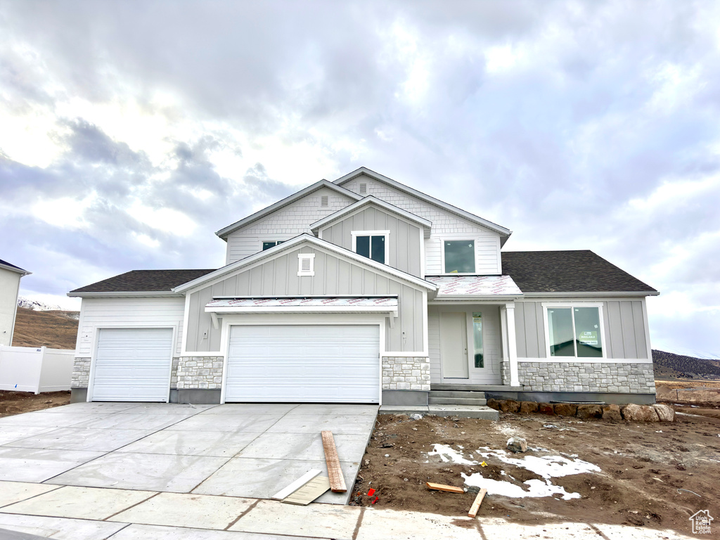 Craftsman inspired home featuring stone siding, board and batten siding, and concrete driveway