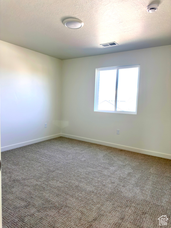 Carpeted spare room with visible vents, baseboards, and a textured ceiling