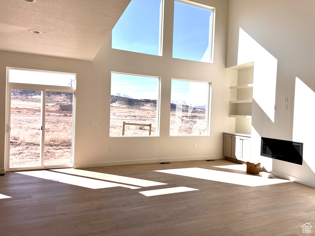 Unfurnished living room featuring a glass covered fireplace, plenty of natural light, a textured ceiling, and wood finished floors