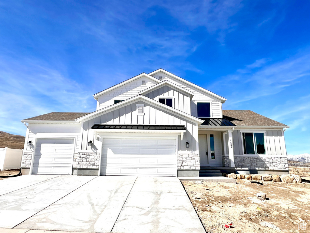 View of front facade featuring an attached garage, board and batten siding, and stone siding