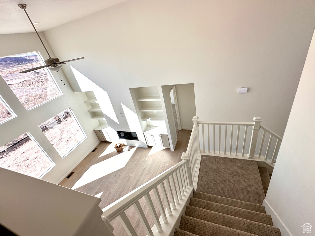 Stairs with baseboards, a high ceiling, ceiling fan, and wood finished floors