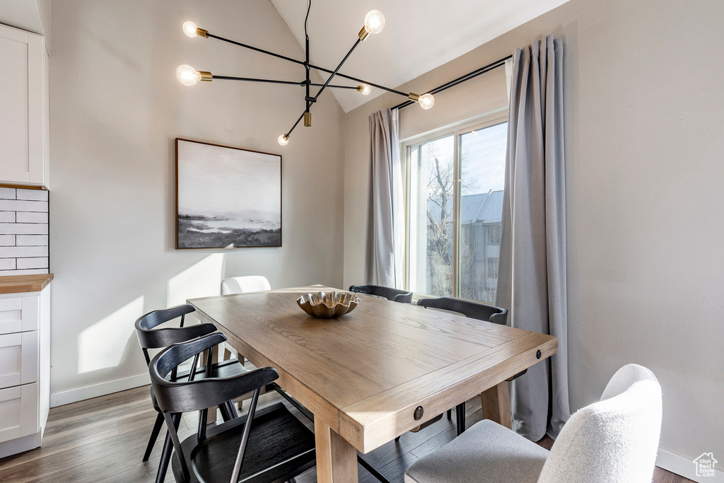 Dining space with a chandelier, vaulted ceiling, wood finished floors, and baseboards