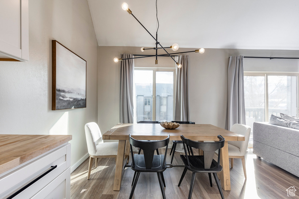 Dining space with a notable chandelier, light wood-type flooring, baseboards, and vaulted ceiling