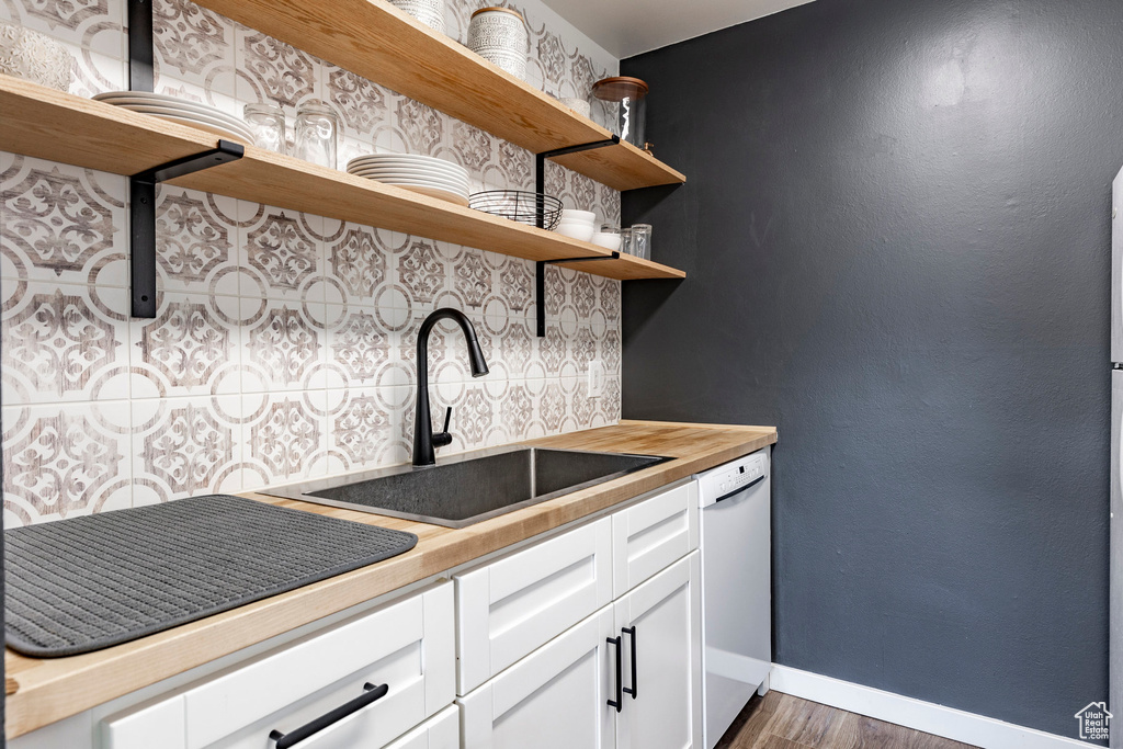 Kitchen with open shelves, a sink, white dishwasher, baseboards, and wood counters