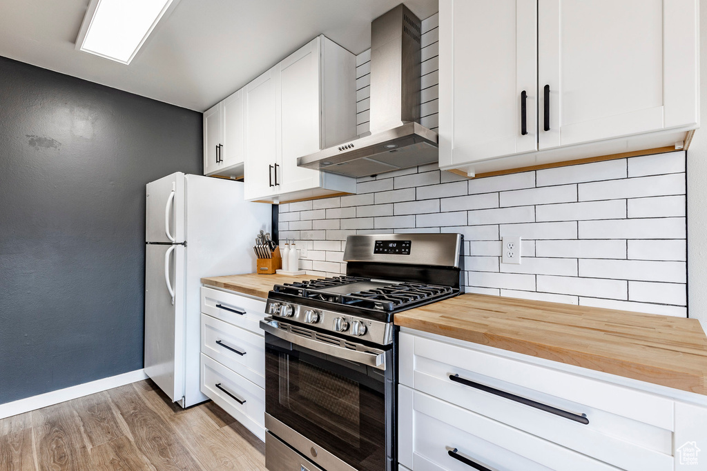Kitchen with stainless steel gas range oven, wood counters, wall chimney range hood, and light wood-style floors