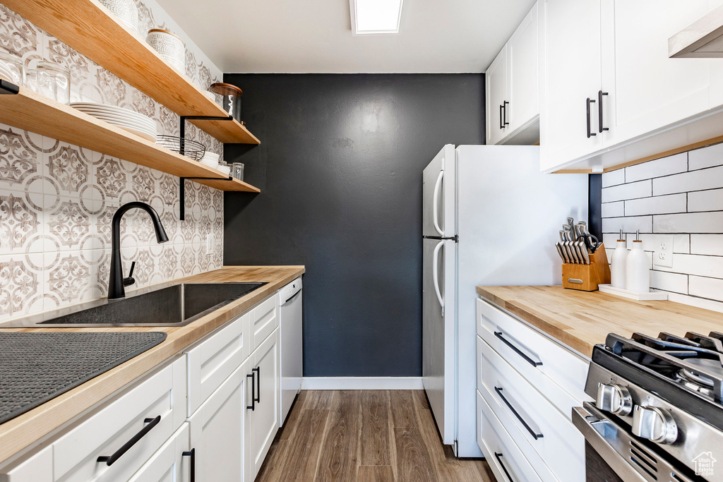 Kitchen featuring open shelves, wood counters, a sink, white appliances, and wall chimney range hood