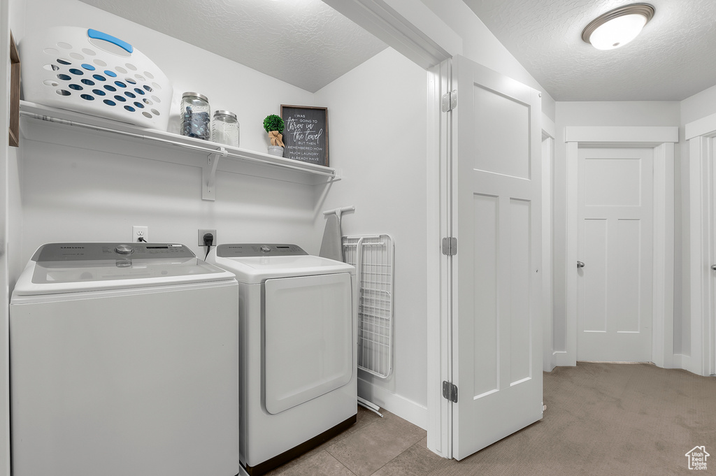 Laundry room featuring a textured ceiling, light carpet, and separate washer and dryer
