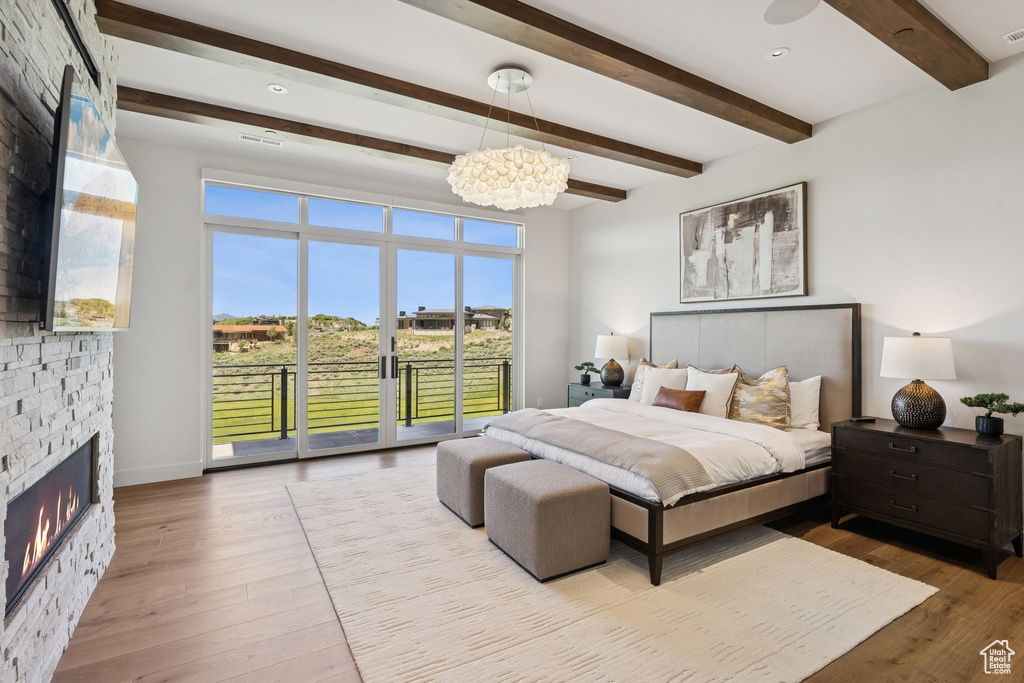 Bedroom with beam ceiling, access to exterior, a chandelier, a stone fireplace, and wood finished floors