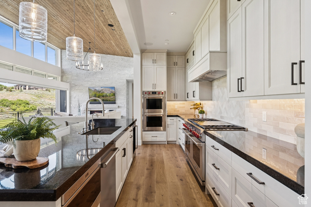 Kitchen featuring stainless steel appliances, dark stone counters, tasteful backsplash, light wood-style floors, and hanging light fixtures