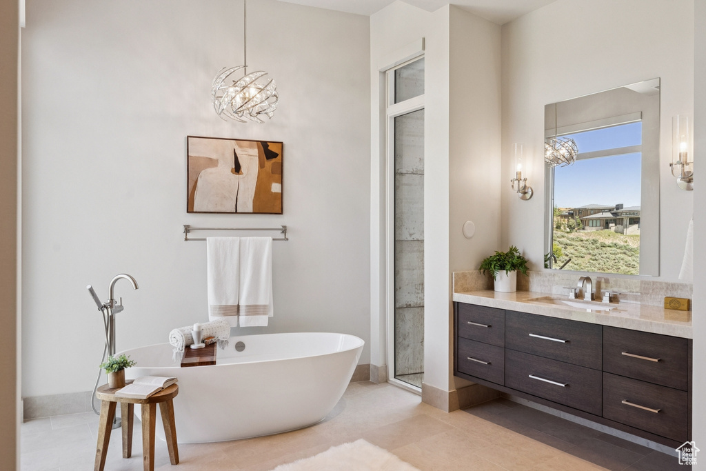 Full bathroom featuring vanity, a chandelier, a freestanding bath, and tile patterned flooring
