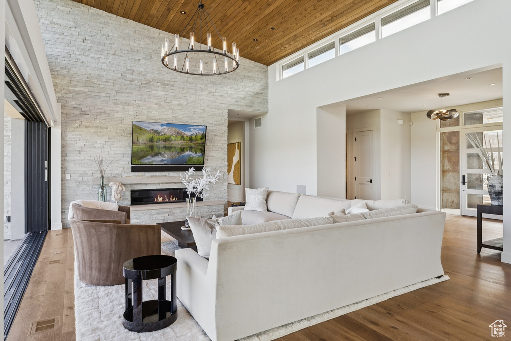 Living room featuring a chandelier, a high ceiling, wood ceiling, a fireplace, and wood finished floors