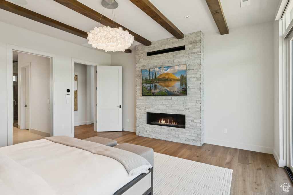 Bedroom featuring a fireplace, a chandelier, beamed ceiling, and light wood-type flooring