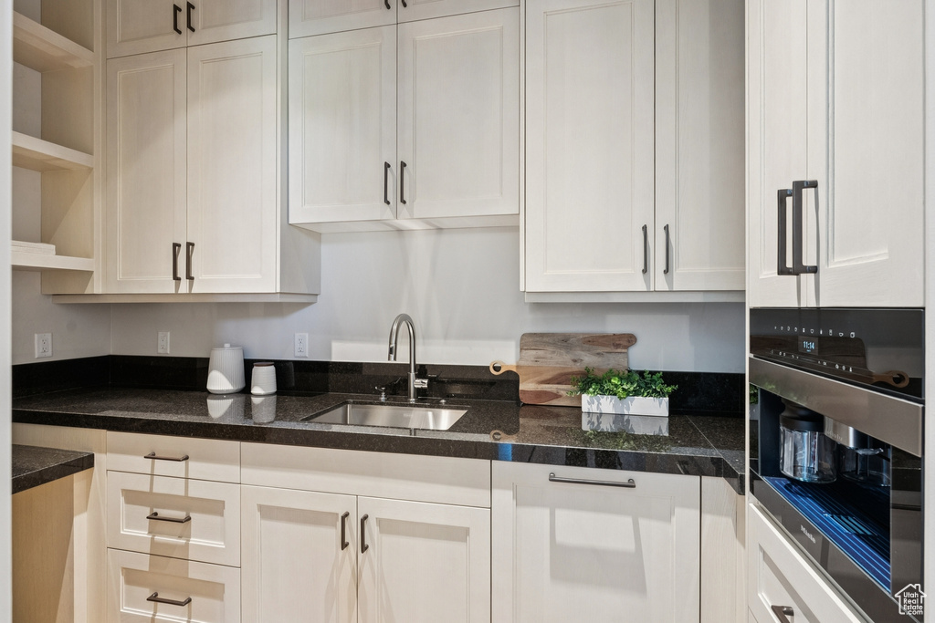 Kitchen with open shelves, white cabinets, stainless steel oven, and dark countertops