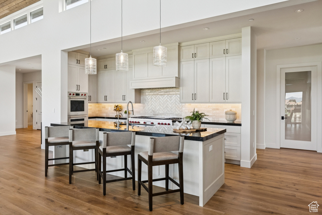 Kitchen with stainless steel double oven, a breakfast bar, dark countertops, tasteful backsplash, and recessed lighting