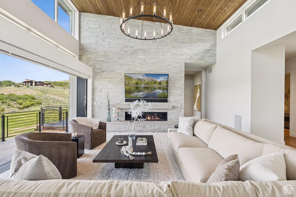 Living area with high vaulted ceiling, wooden ceiling, a chandelier, a stone fireplace, and wood finished floors