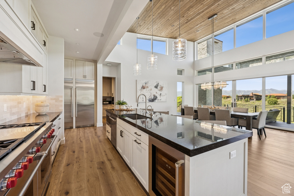 Kitchen featuring custom range hood, premium appliances, dark countertops, wine cooler, and a center island with sink