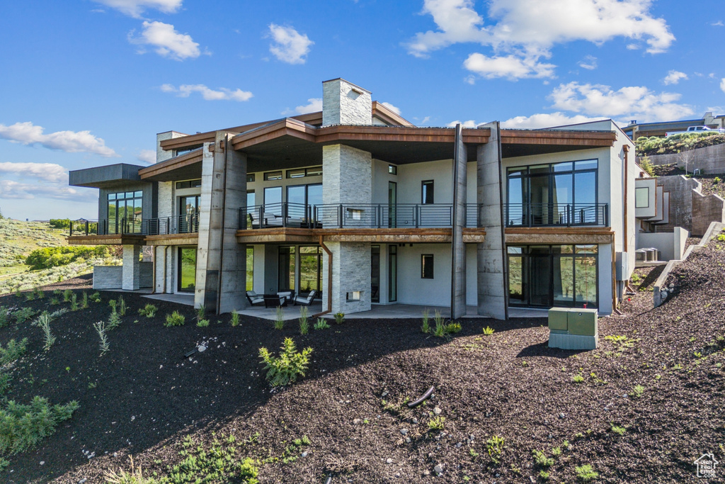 Rear view of house with a balcony, a patio, and a chimney