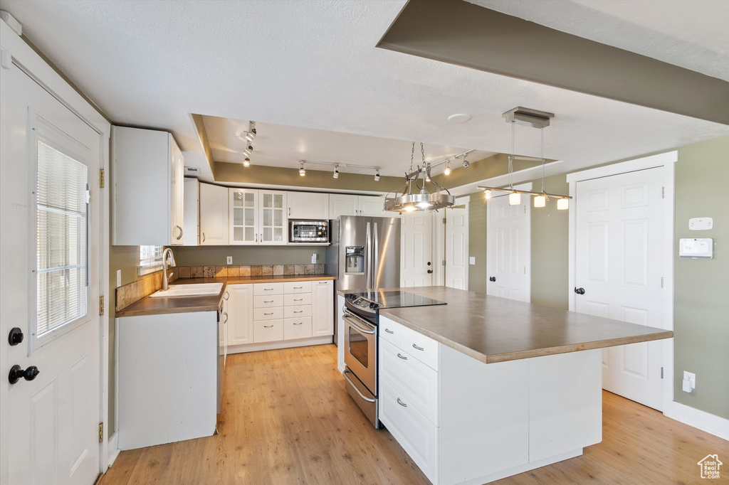 Kitchen featuring appliances with stainless steel finishes, light wood-type flooring, white cabinets, and a sink
