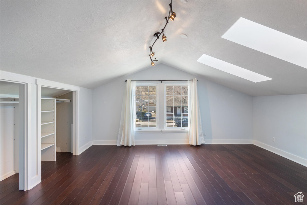 Additional living space with hardwood / wood-style flooring, vaulted ceiling with skylight, baseboards, and a textured ceiling