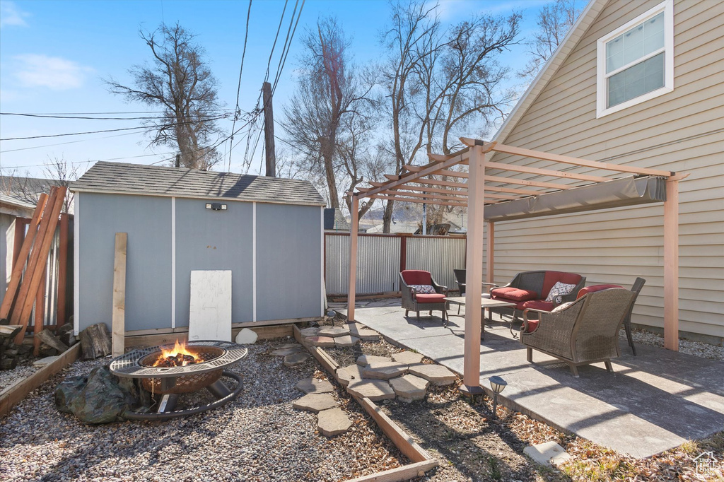 View of patio featuring an outbuilding, a storage unit, a pergola, a fenced backyard, and a fire pit