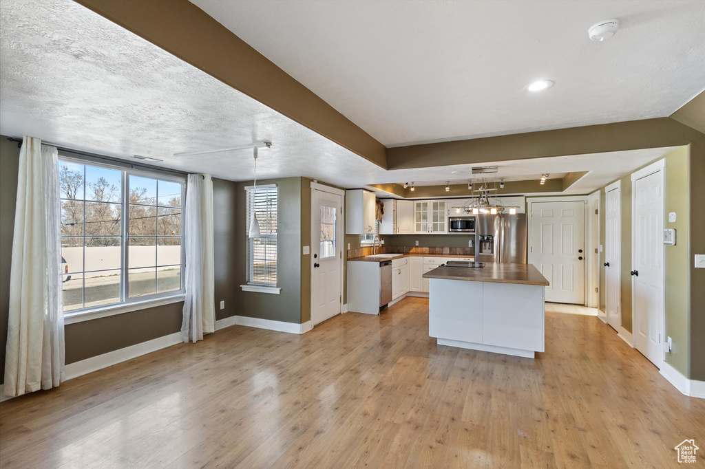 Kitchen featuring light wood finished floors, appliances with stainless steel finishes, glass insert cabinets, white cabinets, and baseboards