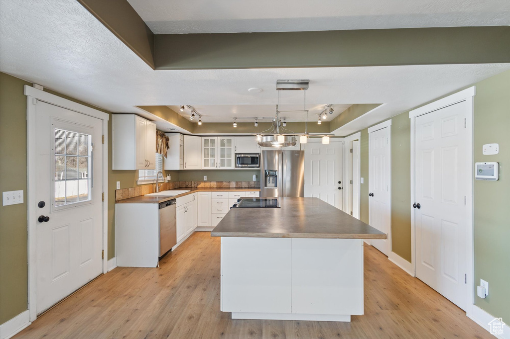 Kitchen with light wood finished floors, stainless steel appliances, white cabinets, a sink, and a kitchen island