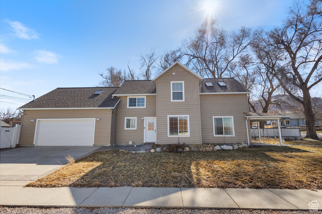 Traditional-style house with a garage, a shingled roof, fence, driveway, and a front yard