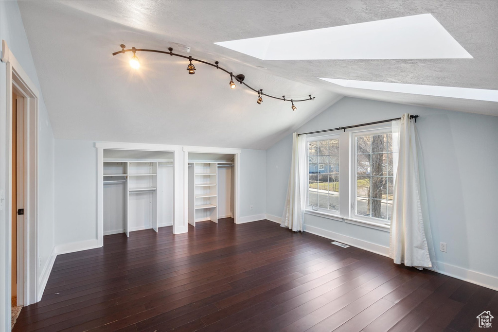 Unfurnished bedroom featuring baseboards, lofted ceiling with skylight, hardwood / wood-style flooring, and multiple closets