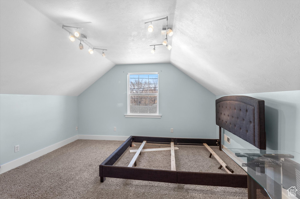 Interior space with lofted ceiling, track lighting, baseboards, and a textured ceiling