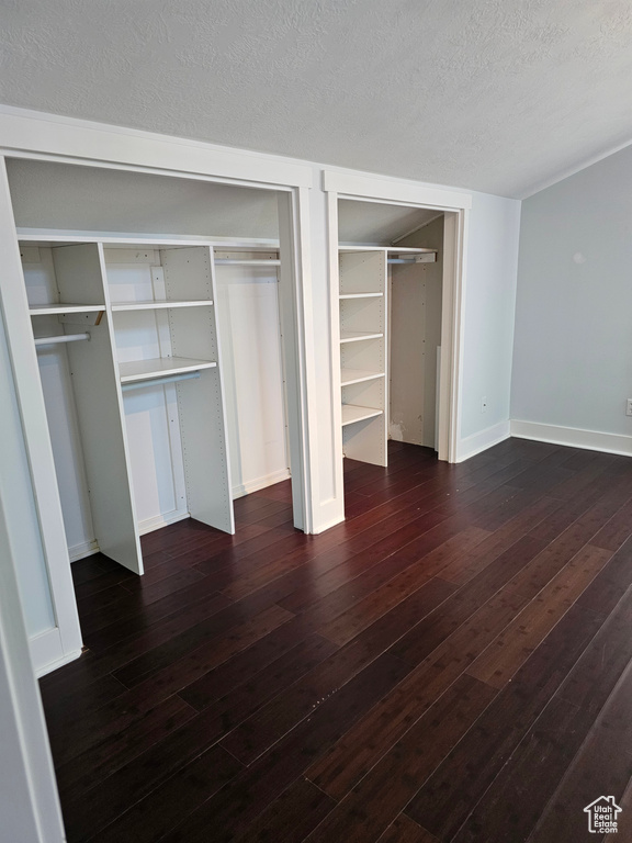 Unfurnished bedroom featuring dark wood-style floors, baseboards, a textured ceiling, and multiple closets