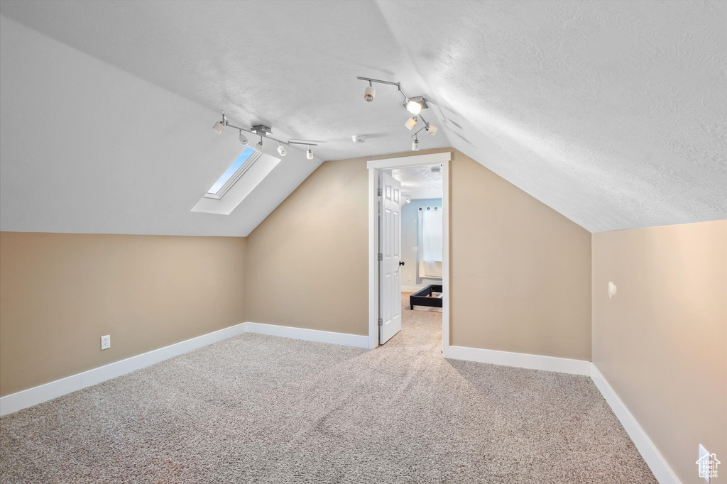 Additional living space featuring vaulted ceiling with skylight, carpet flooring, a textured ceiling, and baseboards