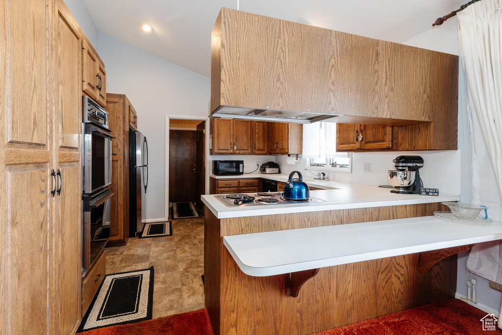 Kitchen featuring a breakfast bar area, stainless steel appliances, kitchen peninsula, and lofted ceiling