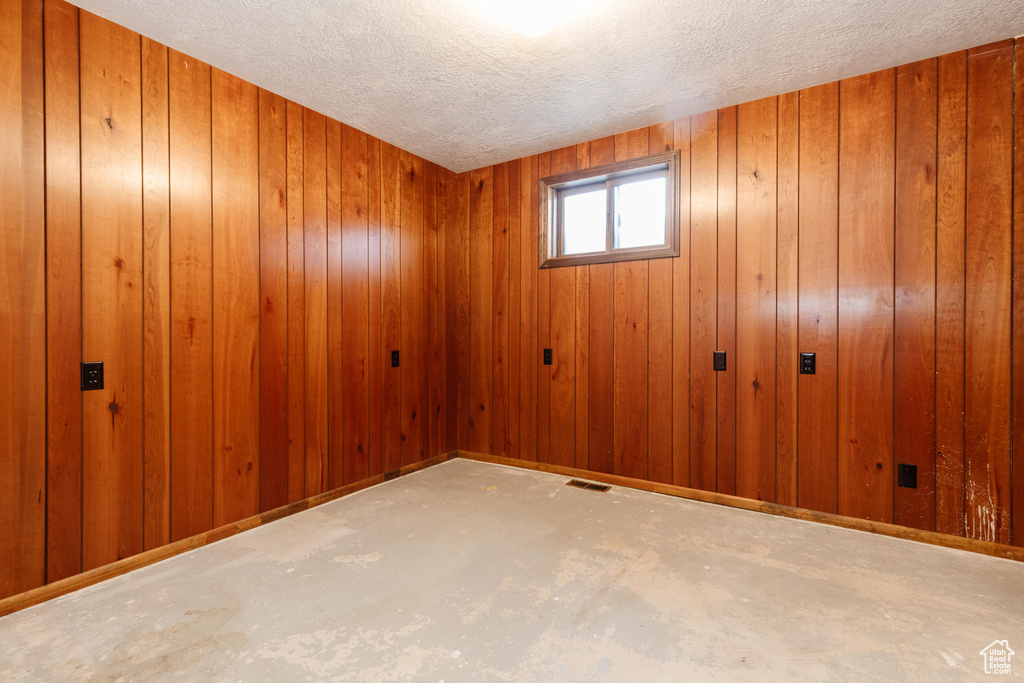 Spare room featuring concrete flooring, wood walls, and a textured ceiling