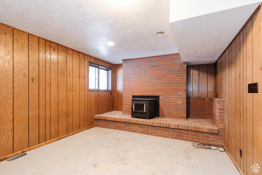 Unfurnished living room featuring a wood stove, wooden walls, and a textured ceiling