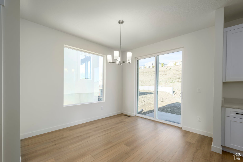 Unfurnished dining area featuring a chandelier and light hardwood / wood-style flooring