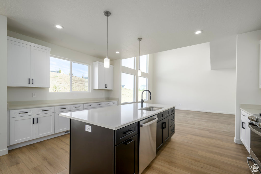 Kitchen with a center island with sink, appliances with stainless steel finishes, light wood-type flooring, pendant lighting, and white cabinets